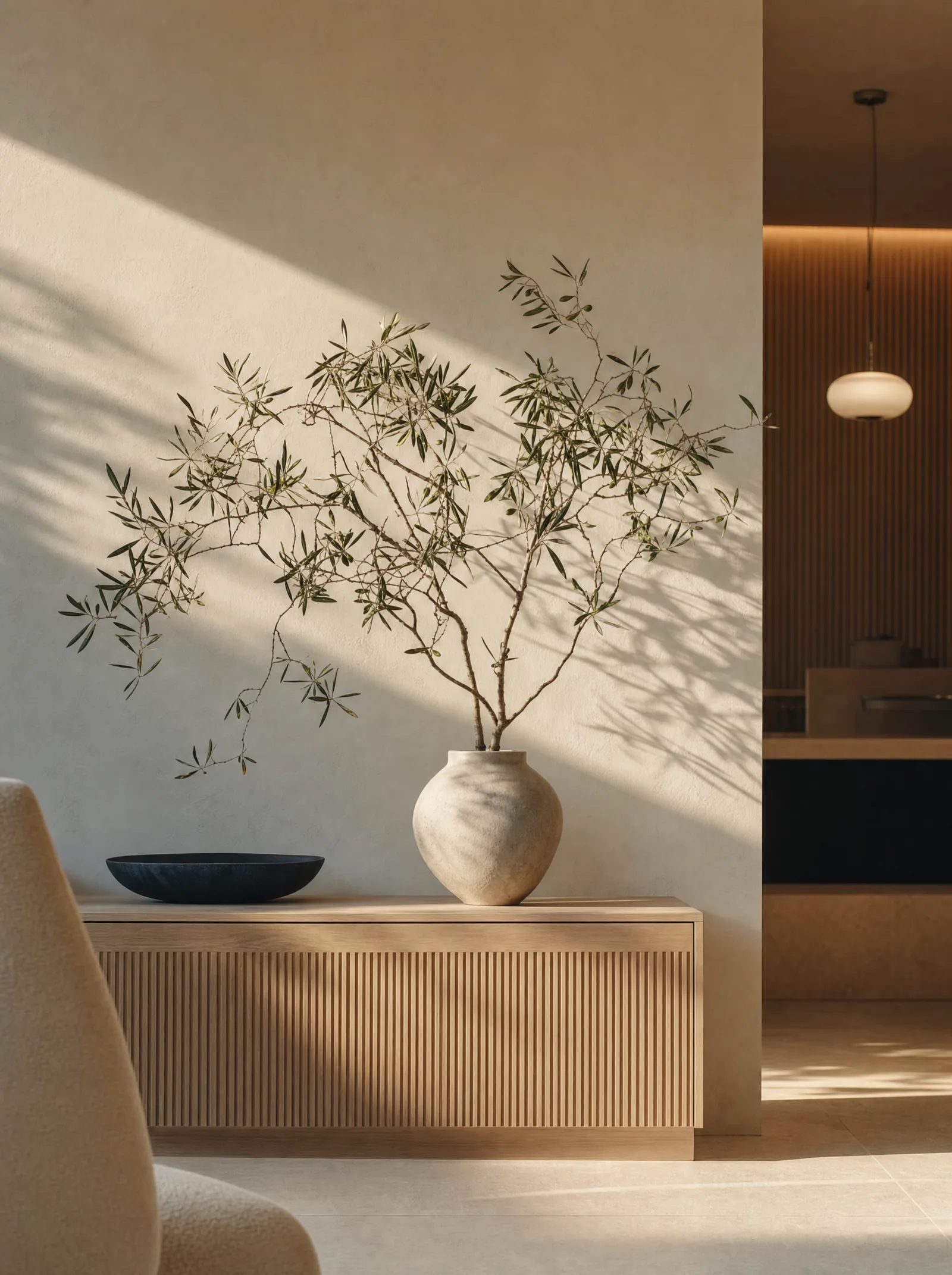 An olive branch in a ceramic vase against a warm plaster wall